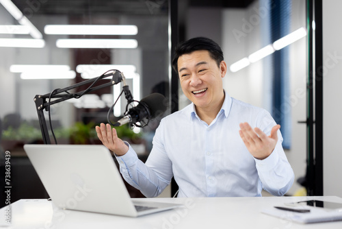Photography An enthusiastic Asian businessman records a podcast in a modern office setting, expressing happiness and professionalism