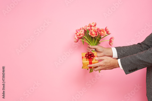 Romantic man presents a gift box and bouquet of tulips on isolated pink background, Valentine's Day, March 8