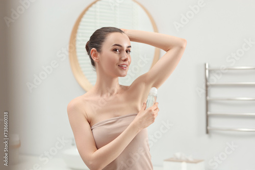 Beautiful young woman applying deodorant in bathroom