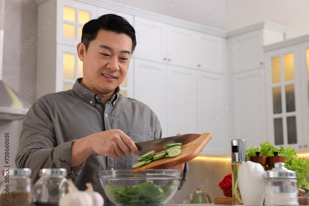 Cooking process. Man adding cut cucumber into bowl in kitchen, low angle view Cooking process. Man adding cut cucumber into bowl in kitchen, low angle view