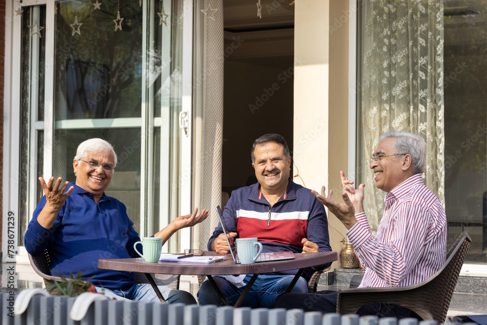 Elderly male friends smiling and reading paper and using laptop. Elderly male friends smiling and reading paper and using laptop.