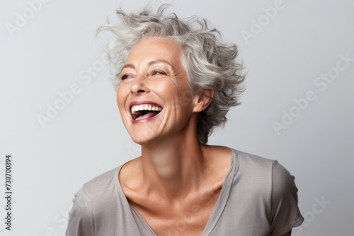 Portrait of a beautiful senior woman with grey hair laughing against grey background