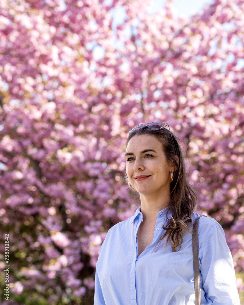 Portrait woman with a smilein a blue shirt on background of blooming pink sakura. Close-up Portrait woman with a smilein a blue shirt on background of blooming pink sakura. Close-up