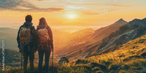 A young couple of travelers stand on a hill and watch the sunset. Hiking tourism concept