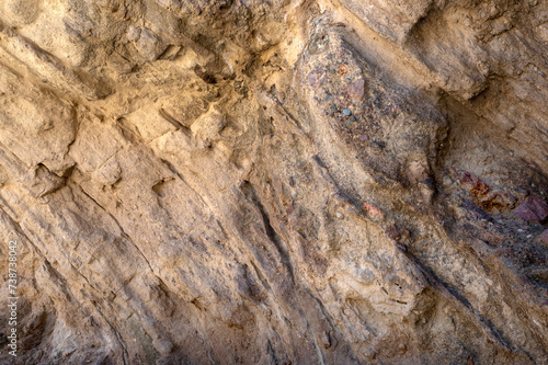 Textured background of rough uneven surface of stone with variety of colors and cracks.