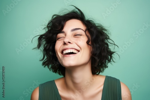 Portrait of a happy young woman laughing with closed eyes over green background © Loli