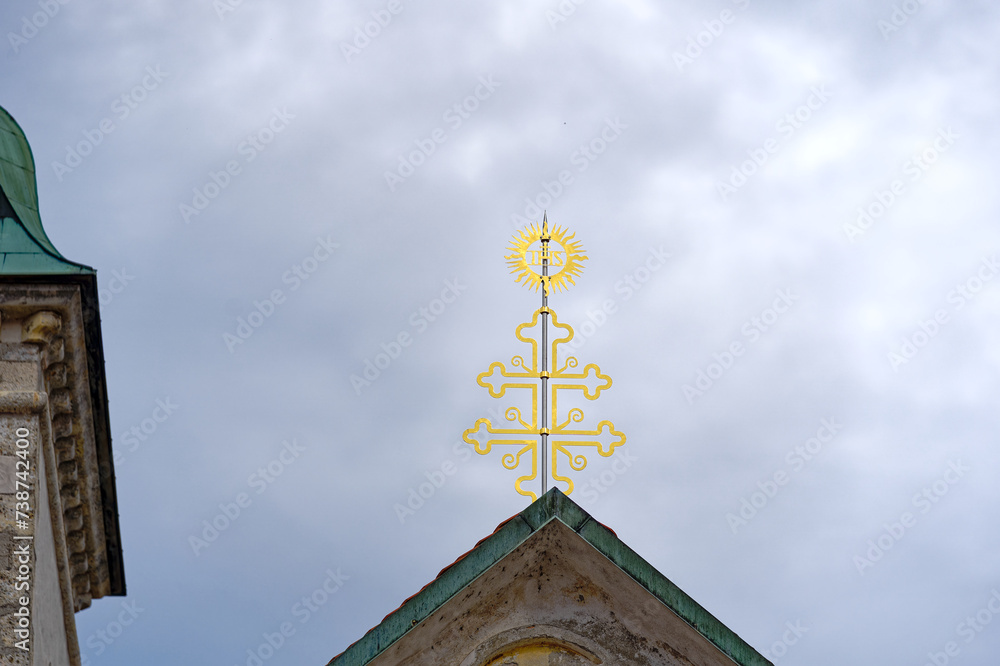 Scenic close-up view of golden cross on top of church at Slovenian City of Skofja Loka on a cloudy summer day. Photo taken August 9th, 2023, Škofja Loka, Slovenia.