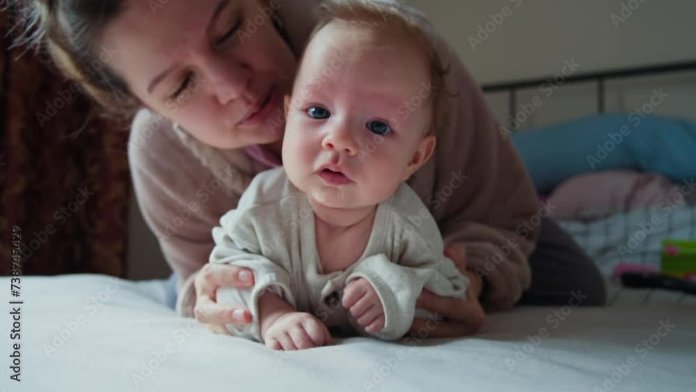 A tender moment between a baby and mum, who is gently kissing the babys forehead. The baby, with striking blue eyes and wisps of light hair, a thread of saliva visible on their chin. A tender moment between a baby and mum, who is gently kissing the babys forehead. The baby, with striking blue eyes and wisps of light hair, a thread of saliva visible on their chin.