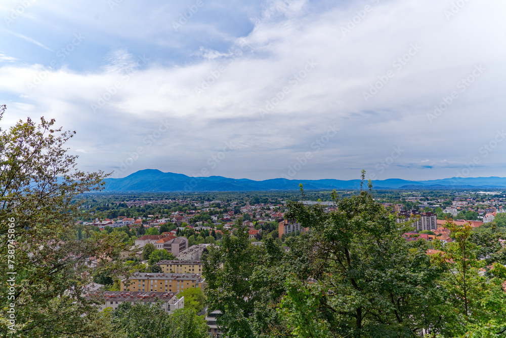 Obraz premium Aerial view of City of Ljubljana seen from Sance castle hill with mountain panorama in the background on a cloudy summer day. Photo taken August 9th, 2023, Ljubljana, Slovenia.