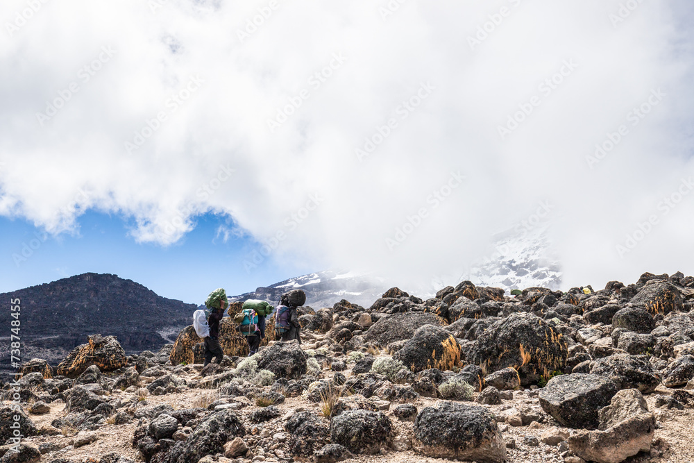 Hikers Ascending Rocky Terrain Amidst Majestic Mt. Kilimanjaro Hikers Ascending Rocky Terrain Amidst Majestic Mt. Kilimanjaro