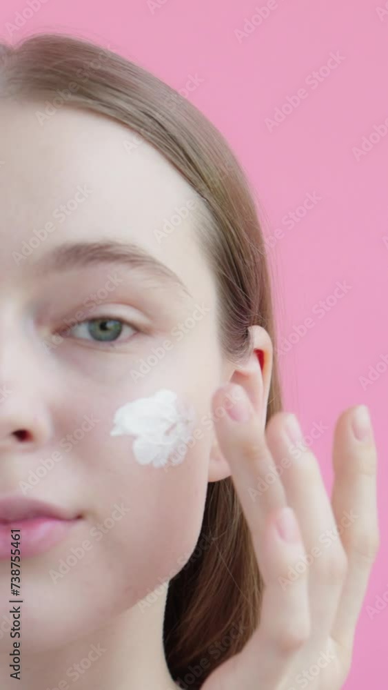 Half face portrait cute young blonde lady on isolated studio pink background, apply moisturizer or sunscreen on cheek, preparation before applying makeup. Concept of skin care ads. Vertical video. Half face portrait cute young blonde lady on isolated studio pink background, apply moisturizer or sunscreen on cheek, preparation before applying makeup. Concept of skin care ads. Vertical video.