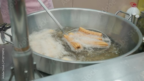 Preparing fried churros. Street food vendor prepares churros inside oily large pan. Churro Spanish and Mexican traditional food photo