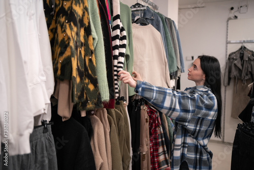 Shopping concept. Young brunette lady picking trendy clothes In fashion store.