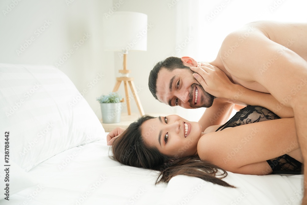 Caucasian handsome man and Asian pretty woman smile while hugging each other in the morning on bed at bedroom white background Caucasian handsome man and Asian pretty woman smile while hugging each other in the morning on bed at bedroom white background