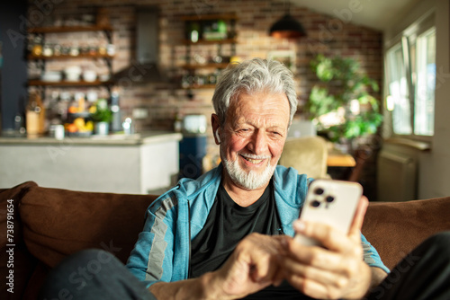 Senior man using a smartphone on the sofa at home photo