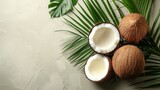 Whole and halved coconuts with lush green leaves on a textured off-white surface, tropical and fresh