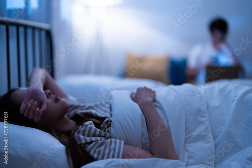 Asian insomnia woman lying awake in bed with a blurred background and frustration of sleepless and restless night because her boyfriend work hard on a laptop before go to sleep
