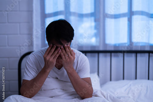 Asian insomnia man covering his face with two hands and massage eyes while sitting on the bed overwhelmed by fatigued and exhausted of disrupted sleep and rest in the bedroom night