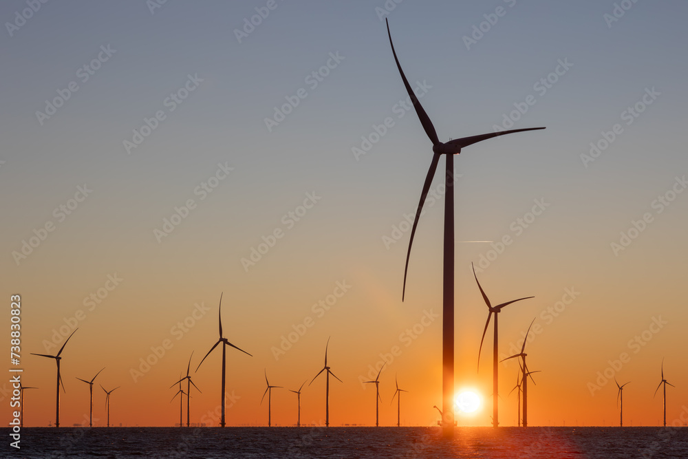 Off shore wind turbines or high, tall wind mills at sea during sunrise 