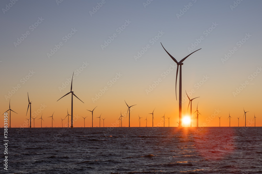 Off shore wind turbines or high, tall wind mills at sea during sunrise 