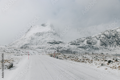 Icy road on Lofoten Islands with snow covered mountains and cloady skies