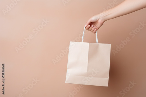 A woman's hand holds a paper bag on a beige background. 