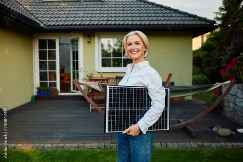Portrait of happy mature woman standing outside her home holding solar panel