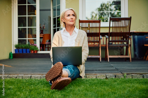 Portrait of mature woman using laptop sitting outside her home at backyard patio
