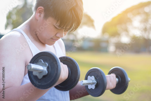 фотографія Young asian plump boy doing exercise with lifting heavy dumbbells in outdoor park in the sunset time of the day, sunlight edited