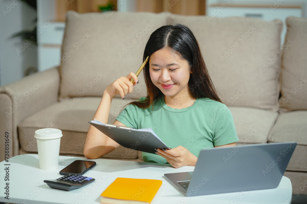 young Asian girl engages in online learning, doing homework on her sofa in the living room. video classes, combining comfort and education at home. young Asian girl engages in online learning, doing homework on her sofa in the living room. video classes, combining comfort and education at home.