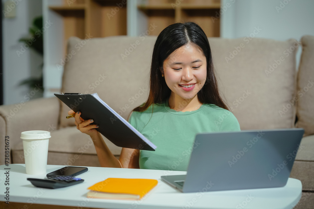young Asian girl engages in online learning, doing homework on her sofa in the living room. video classes, combining comfort and education at home. young Asian girl engages in online learning, doing homework on her sofa in the living room. video classes, combining comfort and education at home.