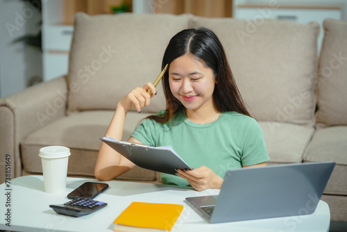 young Asian girl engages in online learning  doing homework on her sofa in the living room. video classes  combining comfort and education at home.