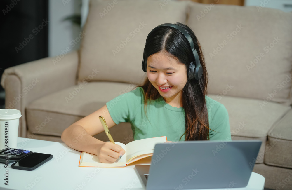 young Asian girl engages in online learning, doing homework on her sofa in the living room. video classes, combining comfort and education at home. young Asian girl engages in online learning, doing homework on her sofa in the living room. video classes, combining comfort and education at home.