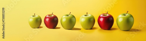 Red and green apples stand on a yellow background in descending order of size. Juicy and ripe fruits. Creative concept of advertising banner. Selective focus. Close-up. Copy space