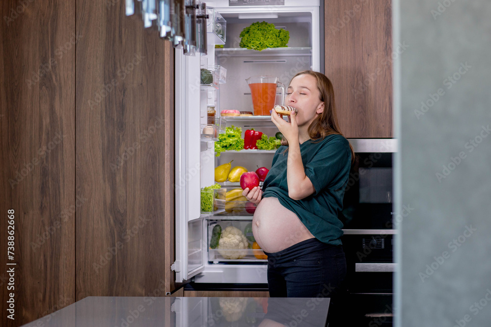 Pregnant woman near the refrigerator eating dessert Pregnant woman near the refrigerator eating dessert