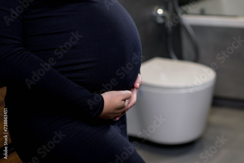 Incontinence and frequent urination during pregnancy. Pregnant woman need to pee standing by toilet in bathroom. Pregnancy concept image. Health and wellbeing of expectant mother