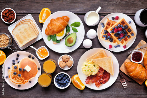 Breakfast or brunch table scene on a dark wood background. Above view. Assortment of sweet and savory food items.