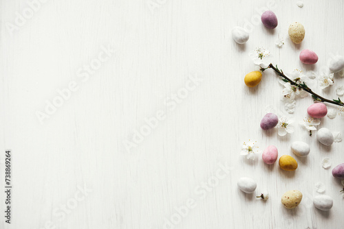 Easter flat lay. Stylish easter chocolate eggs and cherry blossom on rustic white table. Happy Easter! Easter border with space for text. Modern candy colorful eggs and spring flowers