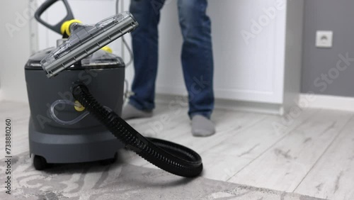 A male cleaning worker assembled a mopping vacuum cleaner for wet cleaning in the room, plugs the wire into the socket. Wet cleaning the room with a professional mopping vacuum cleaner photo