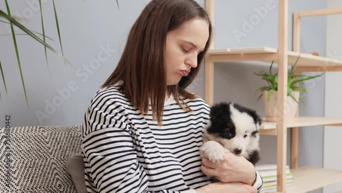 Unhappy Caucasian brown haired woman embracing and petting lonely fluffy small dog with funny spots doesn’t know what to do with the foundling puppy
