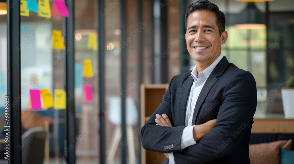 Naklejka premium confident young businessman standing in an office with his arms crossed.