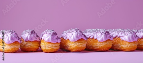 The image features a line of puff pastry-style donuts topped with smooth purple frosting, garnished with white sprinkles that add a touch of contrast. Each donut is delicately layered, showcasing a fl