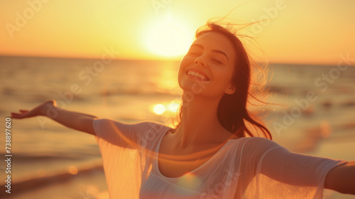 Backlit Portrait of calm happy smiling free woman with open arms and closed eyes enjoys a beautiful moment life on the seashore at sunset