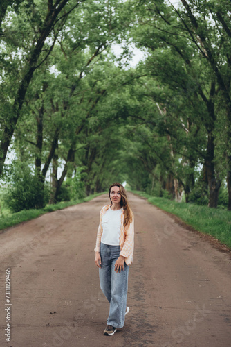 A young girl, a woman walks through a tunnel of green trees. Warm summer day. The girl is dressed lightly. © Ilya.K