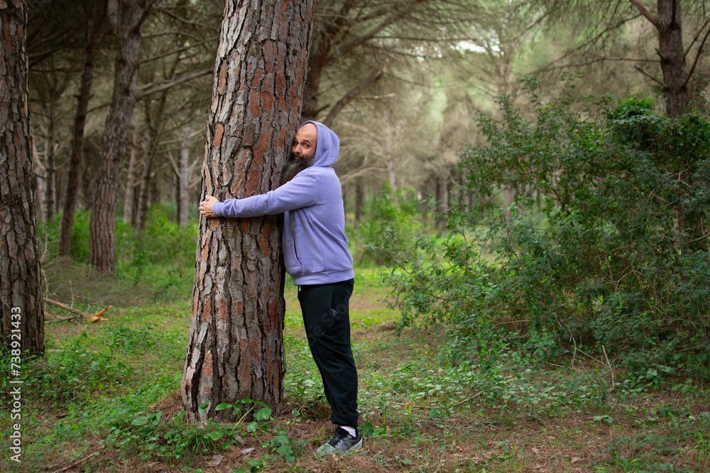 bearded environmentalist in casual clothes, hugging a tree in the woods
