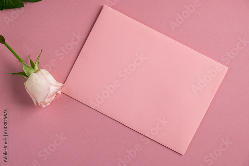 Pink rose on paper pink background next to envelope.