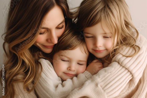 two very young girls snuggle with their mother in a white studio