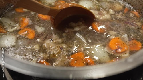 Bone broth with carrots and spices is stirred with a large wooden spoon photo