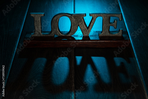 Love, a textured sign in metal, on a wooden table with backlit, cool, blue light.