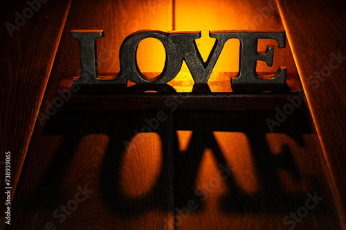 Love, a textured sign in metal, on a wooden table with backlit, warm light..